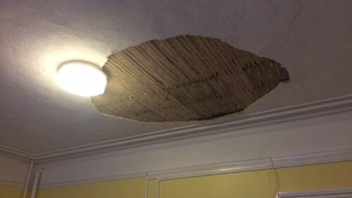 A hole in a ceiling, showing wooden slates, a light, a white ceiling and yellow walls.