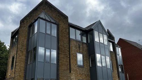 The outside of the office block which has now become apartments, it has black windows and brown brick