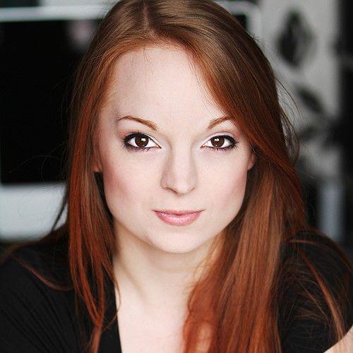 A headshot of a woman with long ginger hair and wearing a black top.