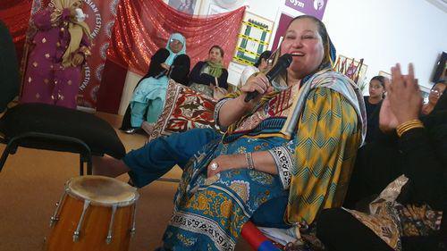 A woman in traditional dress singing while others clap around her