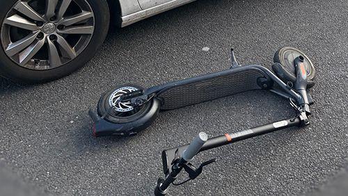 An e-scooter lying on the ground next to a police car.