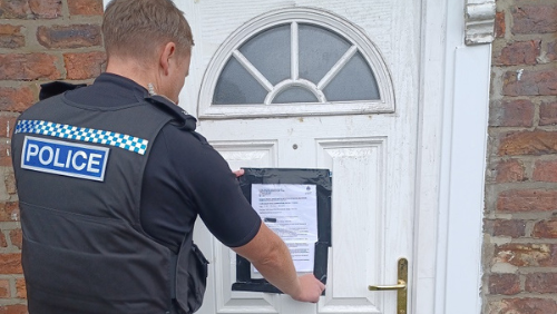 A police officer attaches a notice to a property's front door. The door is white.