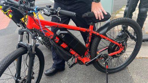 Close-up of the wheels and handles of a red bike, held by a police officer.