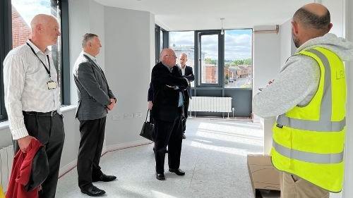 Councillors stood in a bright apartment looking around it, there is also a man in a high vis jacket stood with them looking around the room