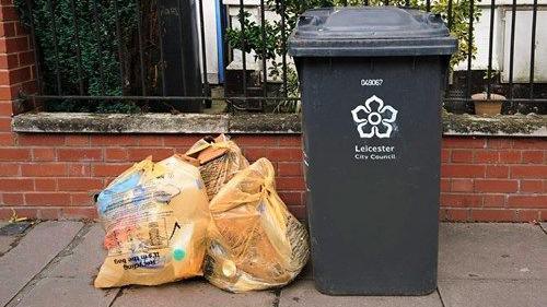 Three orange recycling bags on a pavement next to a black bin with a Leicester council crest