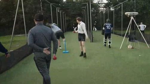 Six players undertake practice in netted areas with a man bowling to a batsman while others watch.