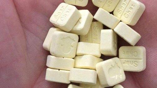 Pile of small, square pale yellow pills in someone's palm.