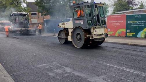 Roads being resurfaced by two resurfacing trucks on a road