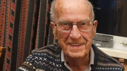 Walter is smiling for the camera. He has wire rim glasses and is wearing a knitted sweater