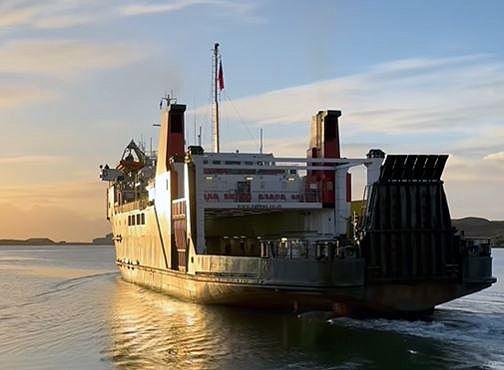 A black and white ship with red funnels, bathed in early morning light, sails away from the camera