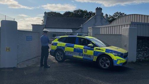 Shows a Garda car and member of An Garda Síochána