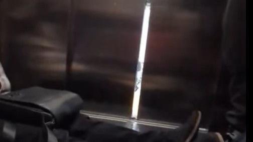 A man sits on the floor inside an elevator, the door is open a short way with light shining through the gap.