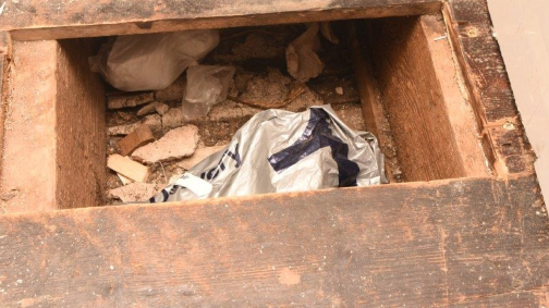 A plastic bag concealed partially concealed below a floorboard, which has been lifted.