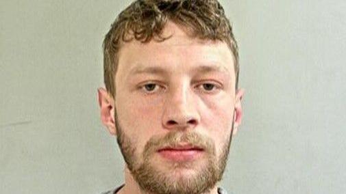 Joshua Tattersall is pictured in a police mugshot. He has short, dark blonde hair which is slightly parted in the middle. He has a dark blonde beard.