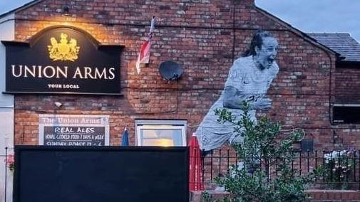 A small brick pub with a black sign that reads 'Union Arms' has a white mural of football player Ella Toone running with her mouth open in excitement