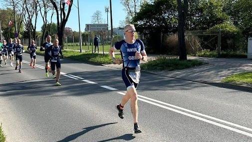 Neil Hunter running in special kit along a road followed by other runners on a sunny day.