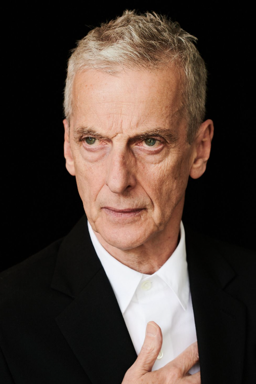 Peter Capaldi looking slightly off camera. He is wearing a black suit and white shirt and has his right hand to his heart