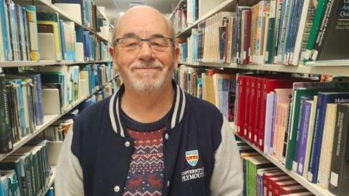 Tony Miller stood in a library and smiling at the camera