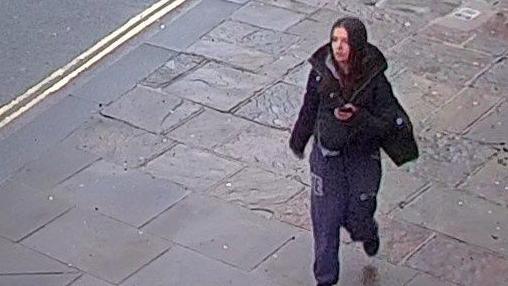 A white girl, about 5ft 4ins tall, with brown hair, wearing a grey hoodie, dark jogging bottoms, black Nike Air Force trainers, and carrying a black bag.