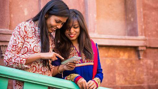 Two young Indian women smile while looking at a funny text message on a mobile phone