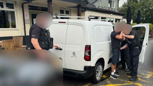 Two police officer can be seen detaining a man by the side of a white van which is parked next to what appears to the the entrance of a pub. Another police officer can be seen with a hand on the handle of the van's read door.