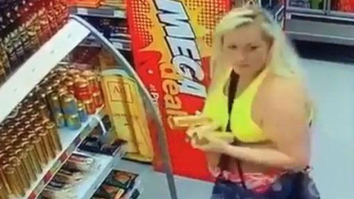 a woman in a jelly crop top is seen with her hands full, carrying pre-mixed vodka drinks she has just taken from a fridge in a store