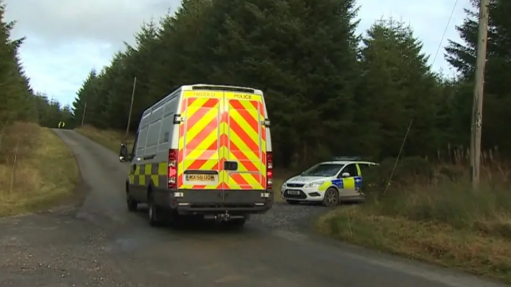 Two police vehicles are parked by a forest, containing large trees