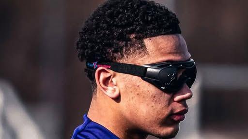 A teenager wears black goggles and a blue top during football training. 