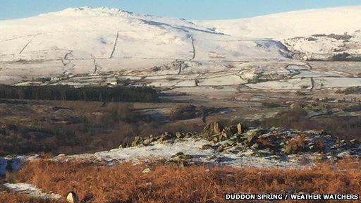 Hills are covered in snow in the distance. In the foreground, lower ground is covered in brown grass