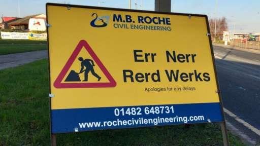 A yellow road sign featuring the triangular red and black symbol for roadworks and black letters reading "Err Nerr Rerd Werks" (Oh no, road works)