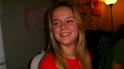 Sofia duke buzëqeshur, duke larguar shikimin nga kamera, e veshur me një bluzë të kuqe. Ajo ka flokë të gjatë e të verdhë. Një llambë është pas saj në të djathtë.