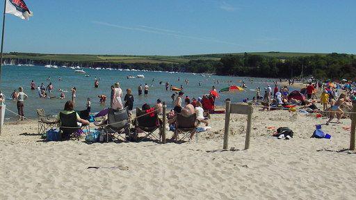 Studland Bay viewed from Knoll Beach on a sunny day, with visitors on the beach and in the water.