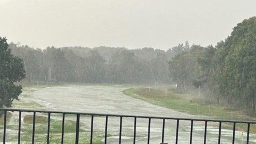 A river of water runs through a fairway on a grassy golf club. There are trees in the background. 