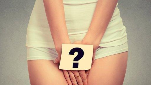 A stock photograph of a clothed woman appearing to put her hands over her genital area - a label with a question marks appears to be stuck on her hand