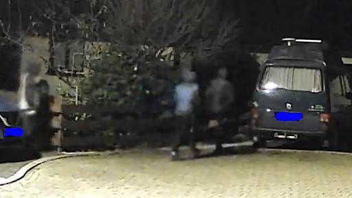 CCTV image shows three individuals in hoodies walking near a parked vehicle. It is dark. The individuals are facing away from the CCTV.