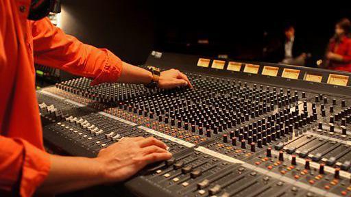 Man in orange shirt twisting black knobs on a grey recording desk