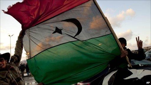 Libyans hold the former royal flag as they drive past a demonstration against Libyan leader Muammar Gaddafi in Benghazi, 27 February 2011