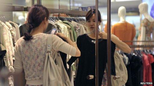 A customer tries a dress in front of a mirror at a shopping mall in Nanjing, Jiangsu province May 29, 2012