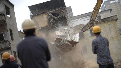 Chinese construction workers oversee a house being demolished