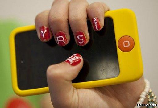 Girl holds up smartphone with Young Rewired State initials painted on her nails