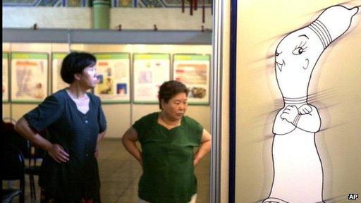 Chinese women walk next to a poster promoting condom use at a sex education exhibition in Beijing