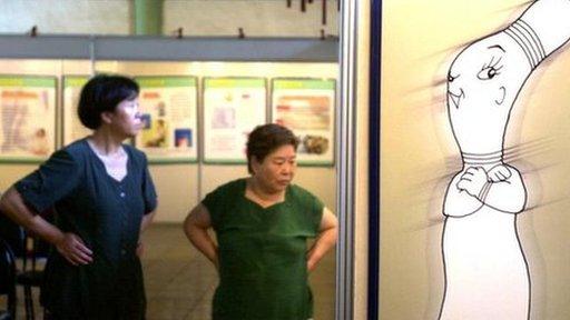 Chinese women walk next to a poster promoting condom use at a sex education exhibition in Beijing