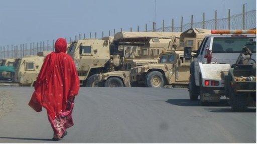 Woman in bright red robes walks past military vehicles in Djibouti