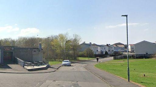 A road with a bar on the left and side and houses 