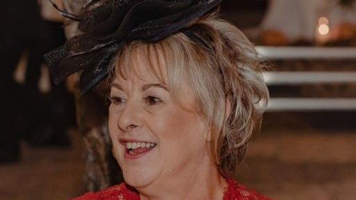 Picture of Karen Kimblin smiling while conversing at an event, wearing a black fascinator and red dress.