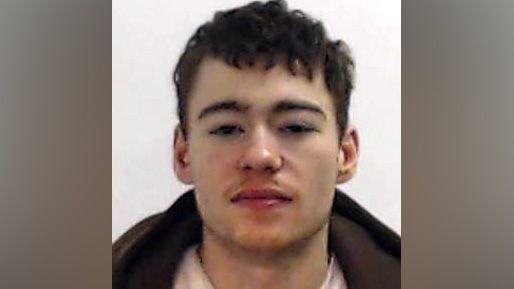 A police mugshot of a convicted domestic abuser, a 22-year-old man with brown hair. 