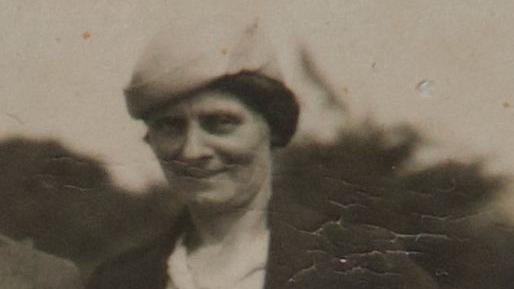 Louisa Dunne in a black and white photograph. She is wearing a hat and a brown jacket with a white shirt.