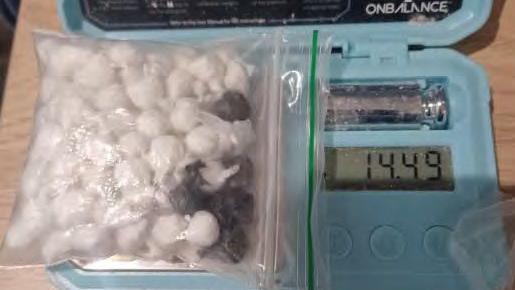 A small set of blue digital scales with a plastic bag on top, which has small, round pouches of drugs