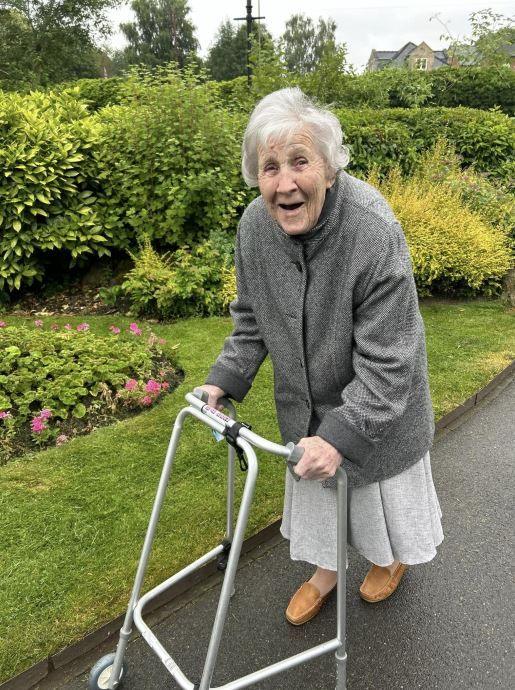 Hilda Jackson walking with a frame along a path in some gardens