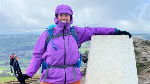 Rebecca Dawson wearing a purple outdoor coat, standing at the top of a hill next to a plinth.